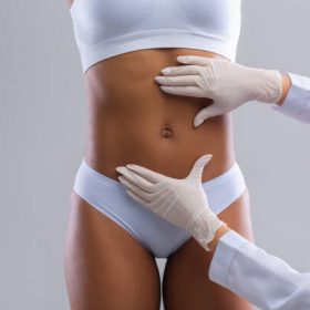 Cropped of plastic surgeon hands checking afro woman belly before beauty procedure, liposuction concept